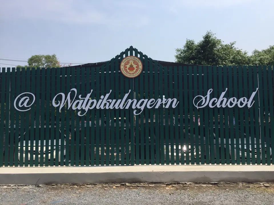 ตัวอักษรชื่อโรงเรียนกับตราโรงเรียน ติดบนรั้วสีเขียว
